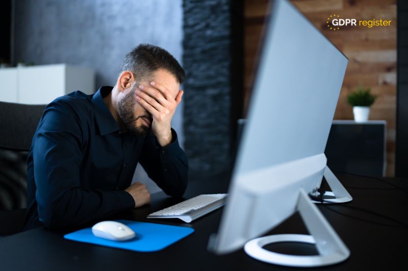 Stressed businessman with hand on face in front of a computer, illustrating the challenges of managing data breaches in small businesses