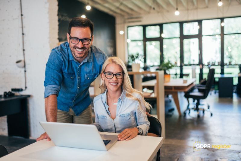 Smiling business partners in a modern office working on a laptop, representing teamwork in preparing a small business for GDPR compliance